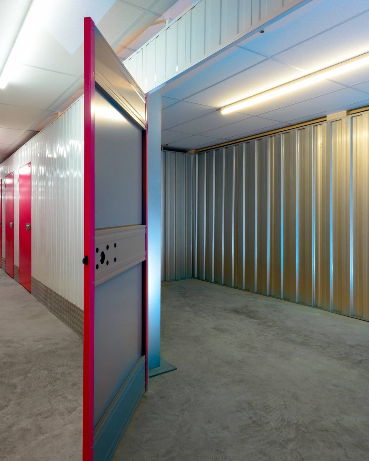 An empty storage unit with its door open, beside a corridor of units at The Store Room Solihull